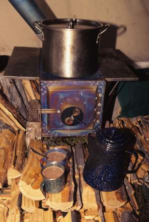 A titanium stove is the heart of a warm tent. Adjacent firewood reflects the heat into the living space and prevents melt-back around the stove. With good wood and the stove cranked up, the tent's ridgeline is about 130°F, living level 75-80°F, and the kitchen pit floor about 50°F. Flat firewood provides a bit of warm 