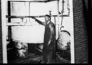 A worker poses by an acid still. He’s covered in charcoal soot, probably surrounded by asbestos. 